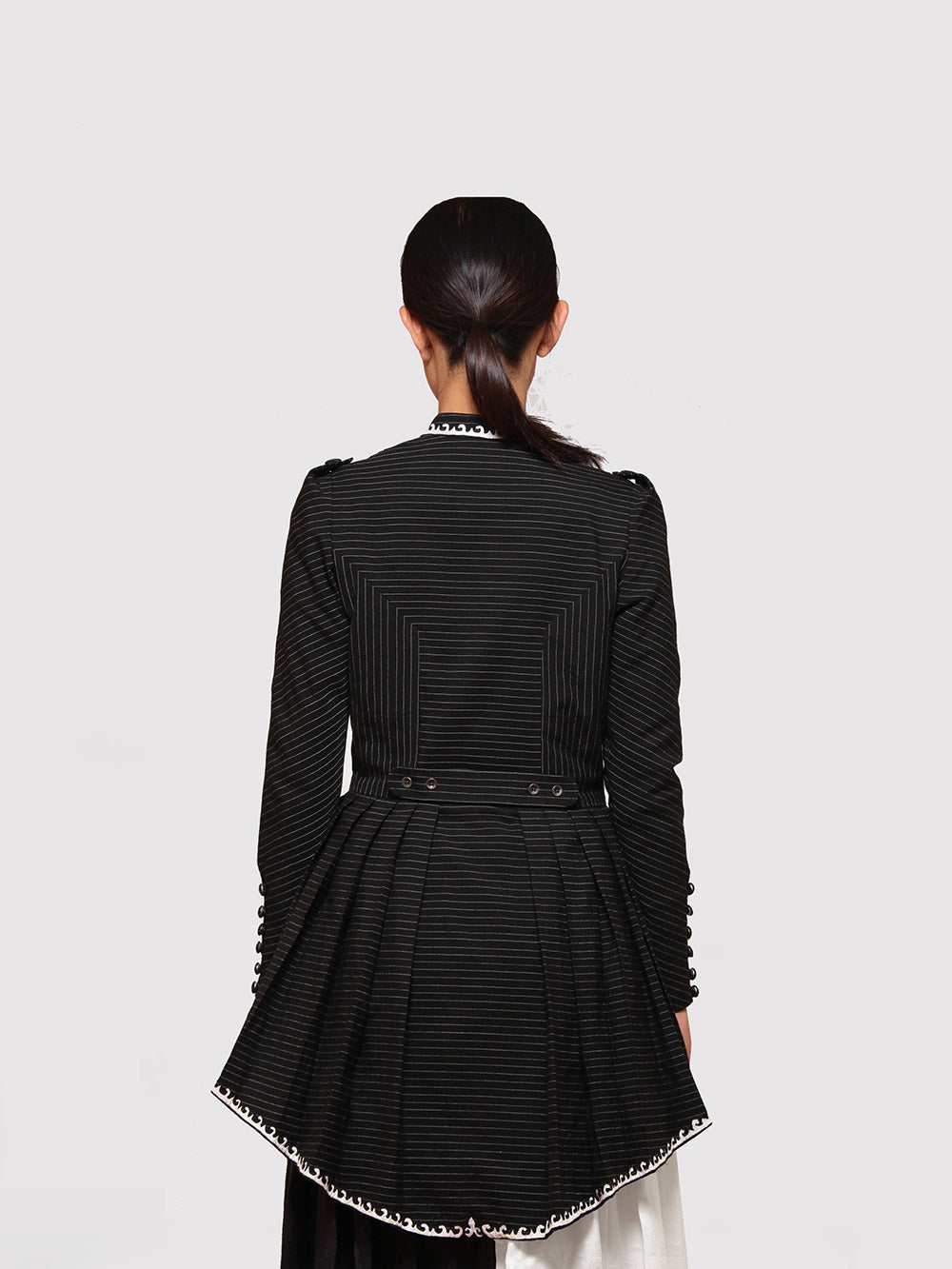 Back view of model posing with Black and gold stripe High- low tiered Jacket with applique work designed by Khumanthem Atelier