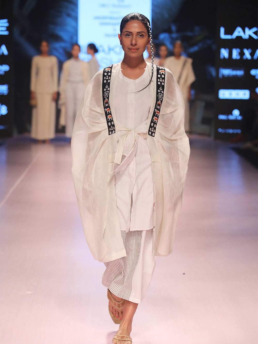 Ramp walk view of model wearing Back view of hanger shoot of Unbleached white colour Cocoon coat with tie-up front (traditional Shamee-Lanmee Motif of Meitei), designed by Khumanthem Atelier, during Lakme Fashion week, 2018